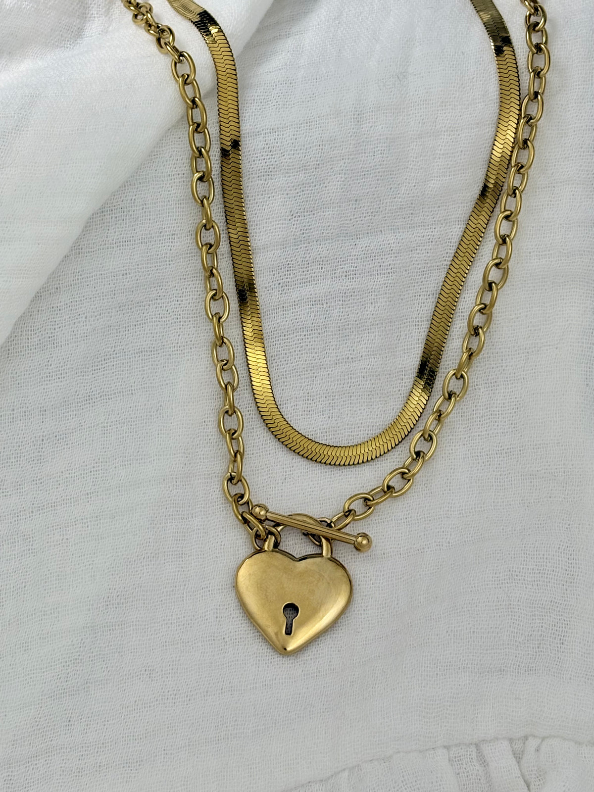 Gold chain necklace with a heart-shaped padlock pendant on a white fabric background
