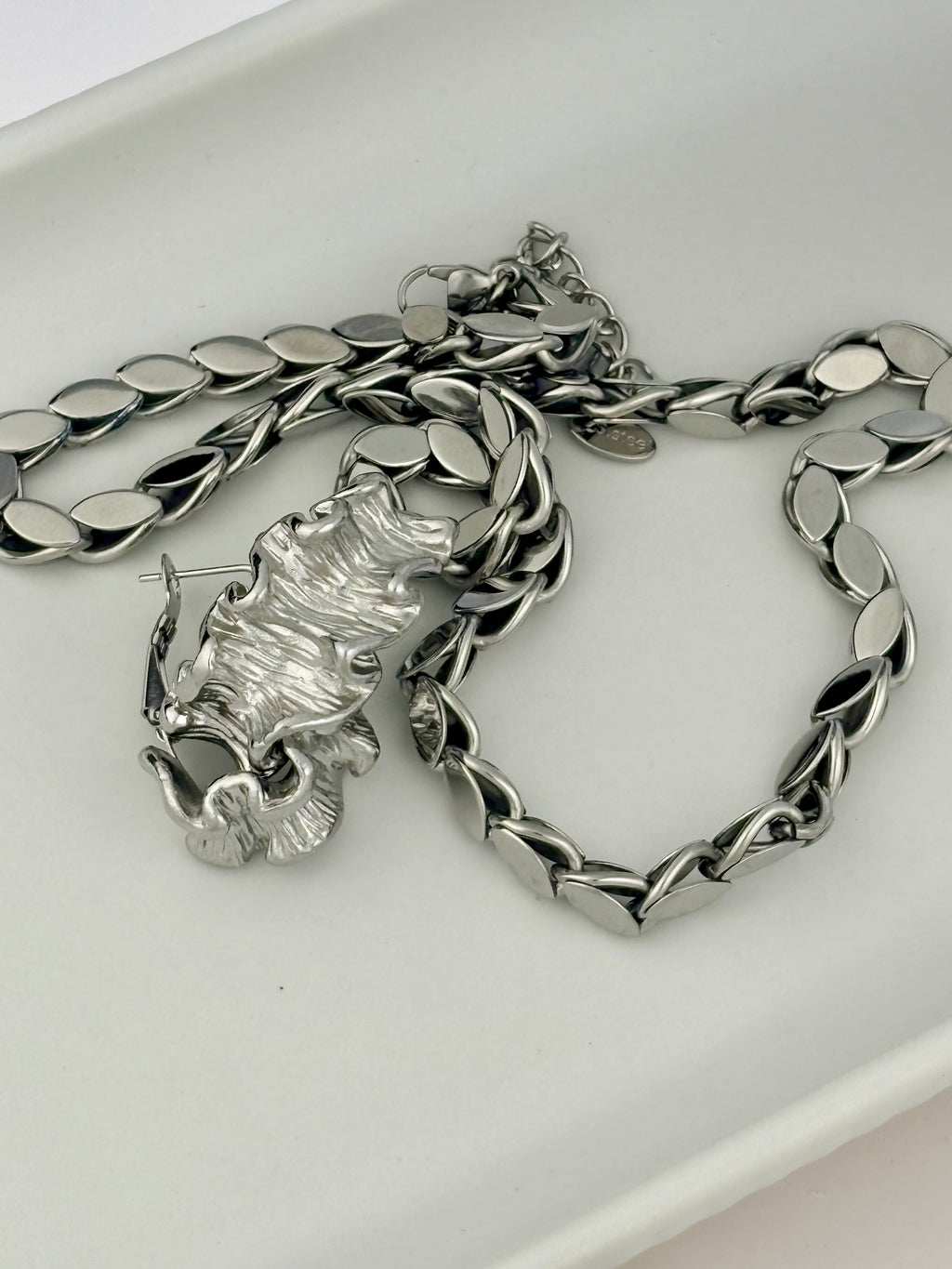 Silver chain necklace and earrings on a white surface