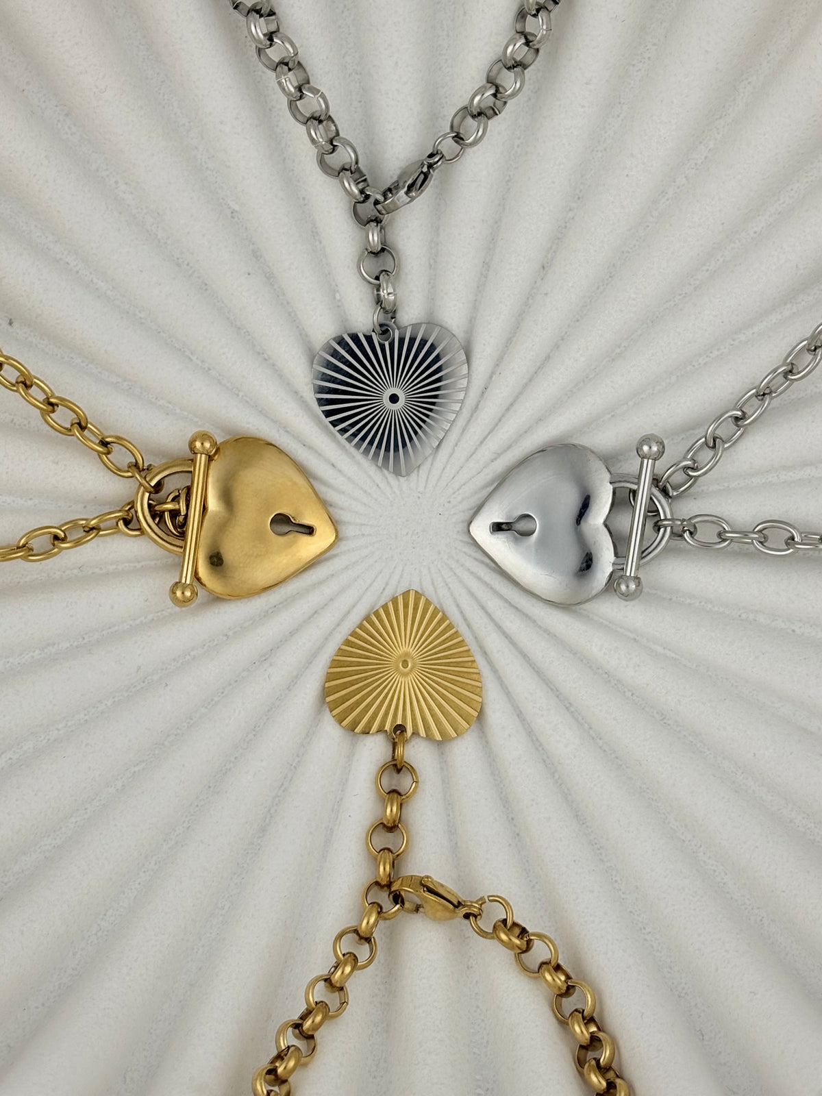 Four heart-shaped pendants on chains arranged in a circular pattern on a textured white background.