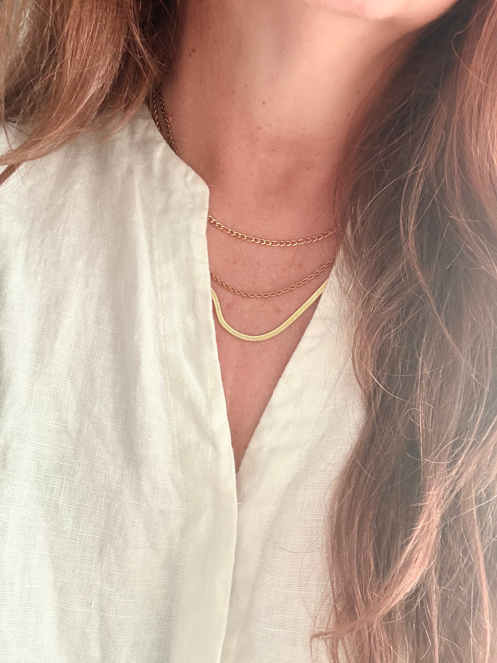 Close-up of a person wearing a delicate gold necklace on a white fabric background