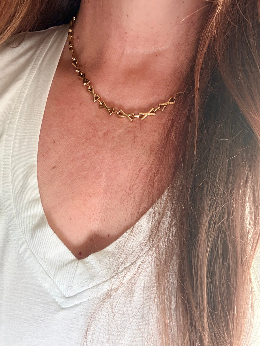 Close-up of a gold chain necklace on a person wearing a white shirt.