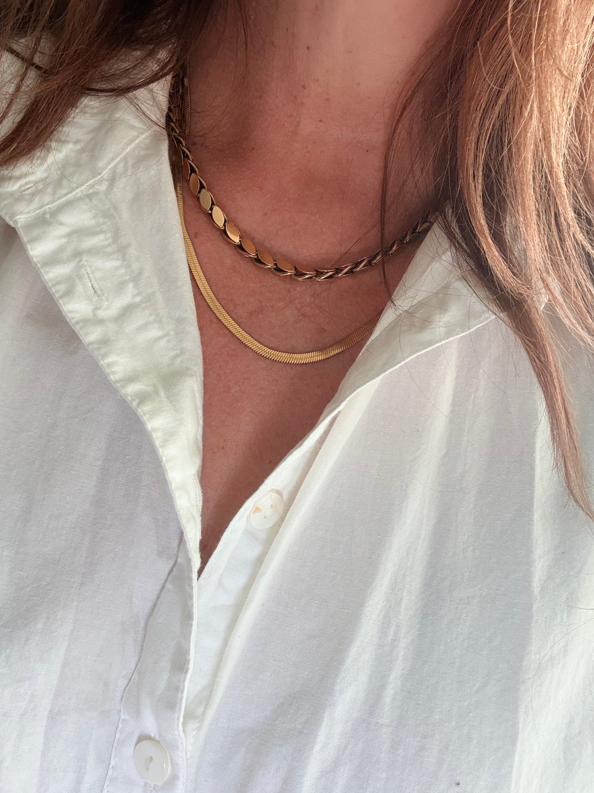 Close-up of a person wearing a gold necklace with a white shirt.