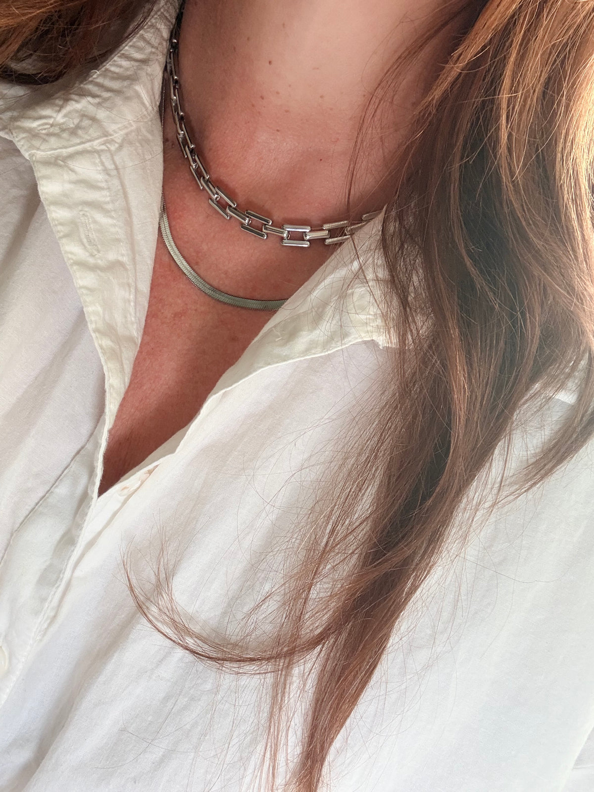 Person wearing a white shirt and silver necklace stack