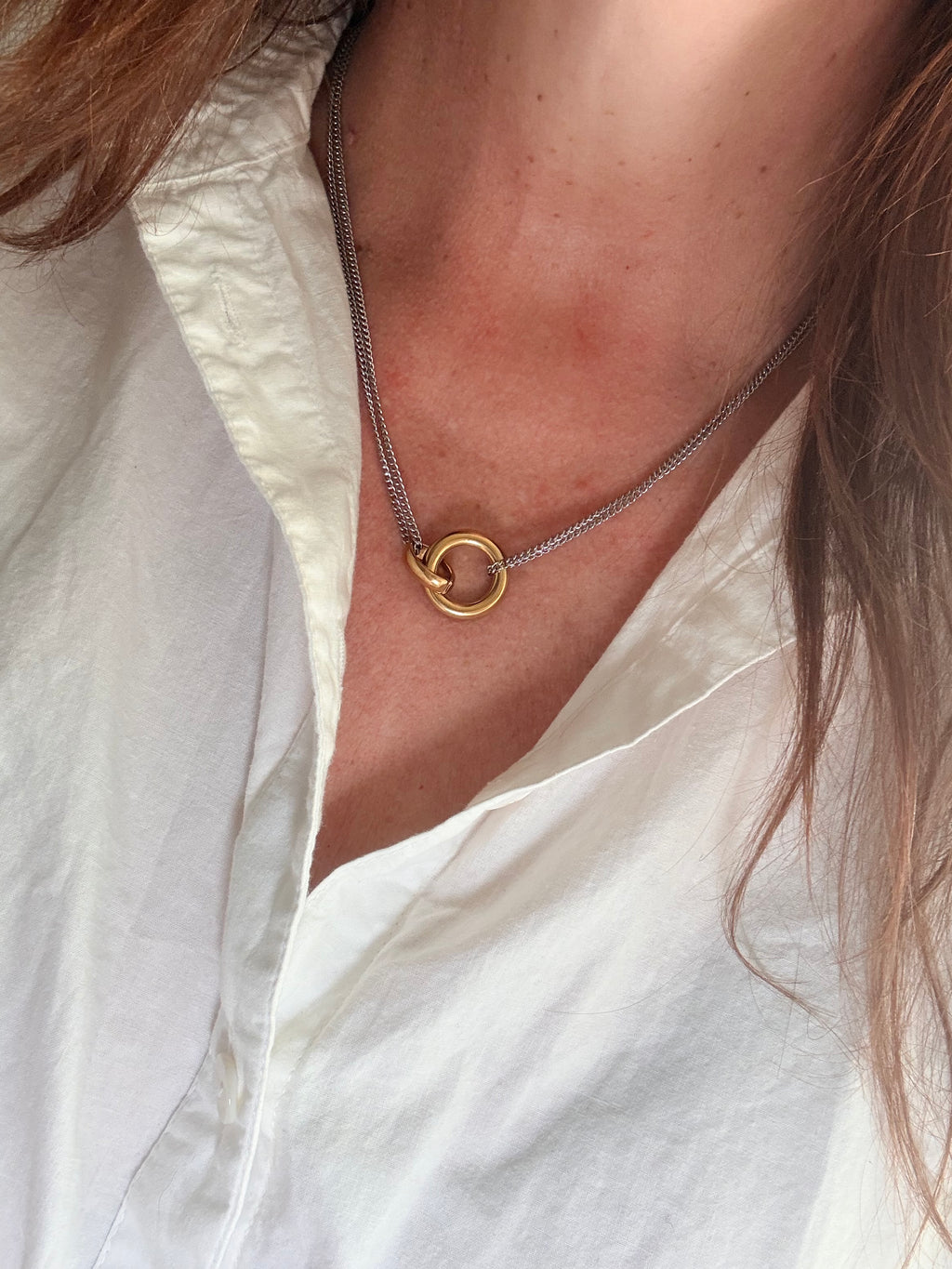 Close-up of a gold necklace with a circular pendant on a person wearing a white shirt.