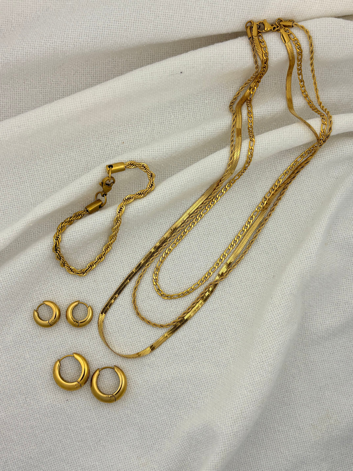 Gold jewelry set including necklaces and earrings on a beige fabric background
