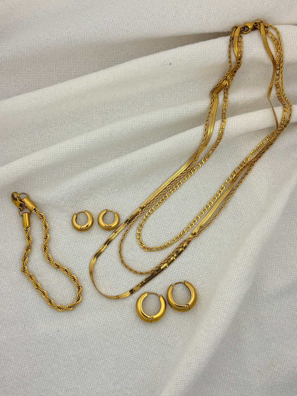 Gold jewelry set including necklaces and earrings on a white fabric background