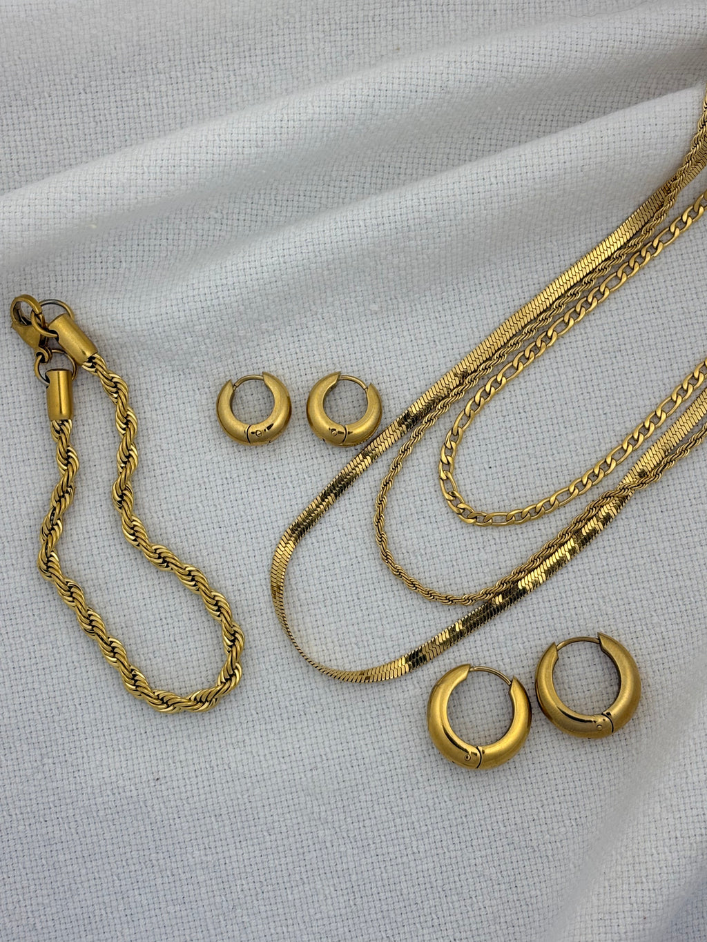 Gold jewelry including necklaces and earrings on a light fabric background