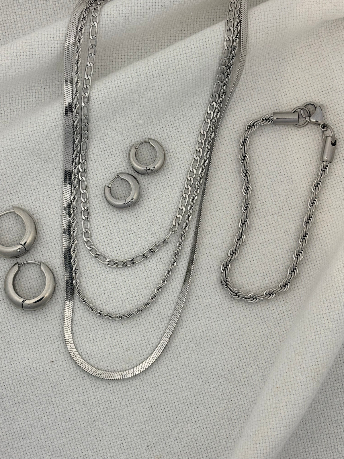 Silver chain necklace and earrings on a textured fabric background