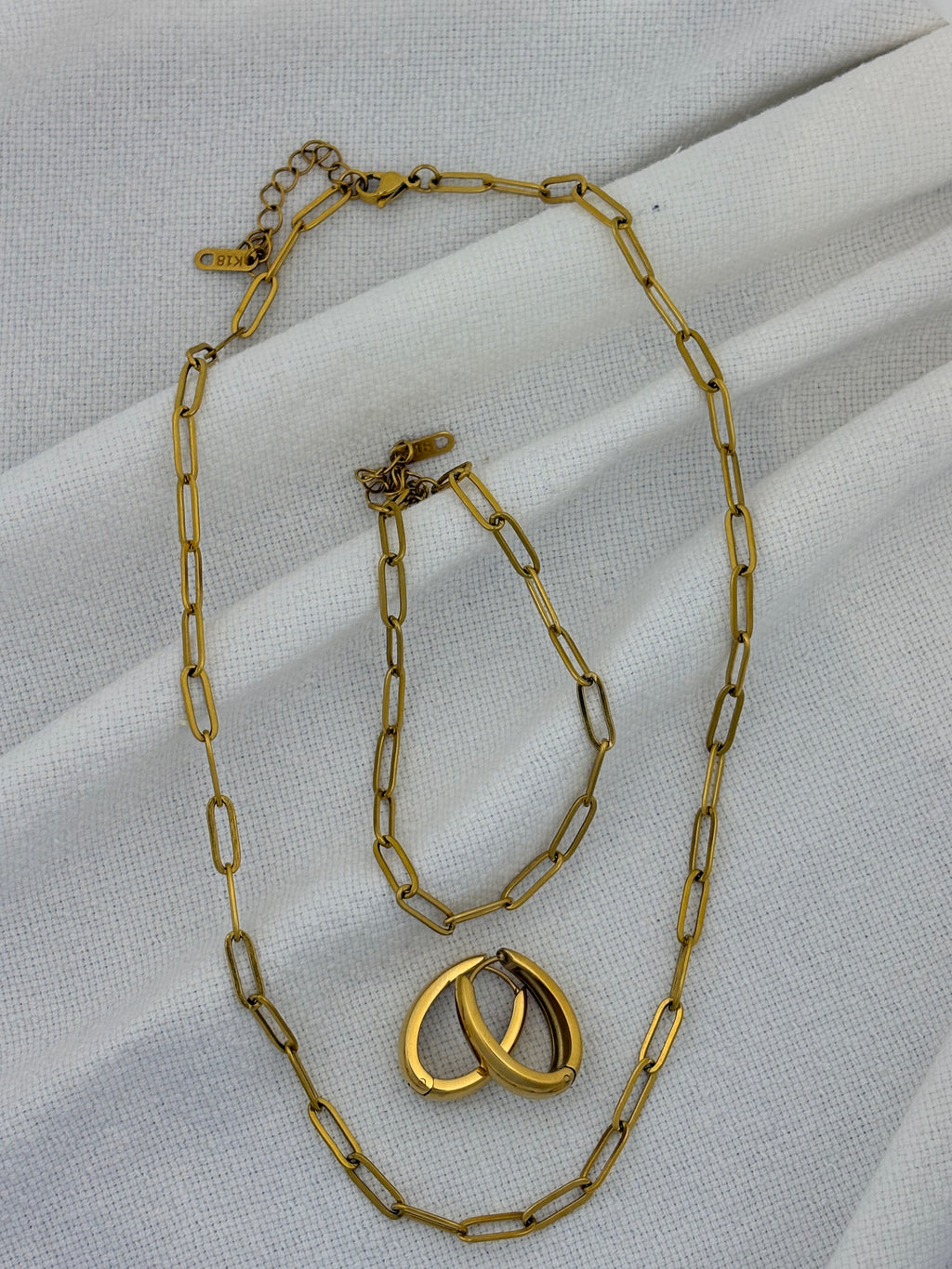 Gold chain necklace, bracelet and earrings on a white fabric background