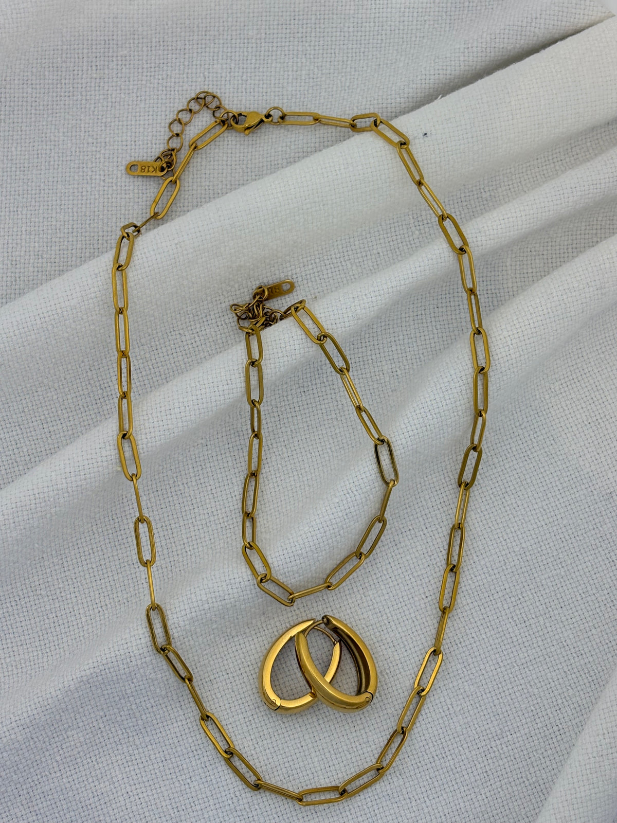 Gold chain necklace, bracelet and earrings on a white fabric background