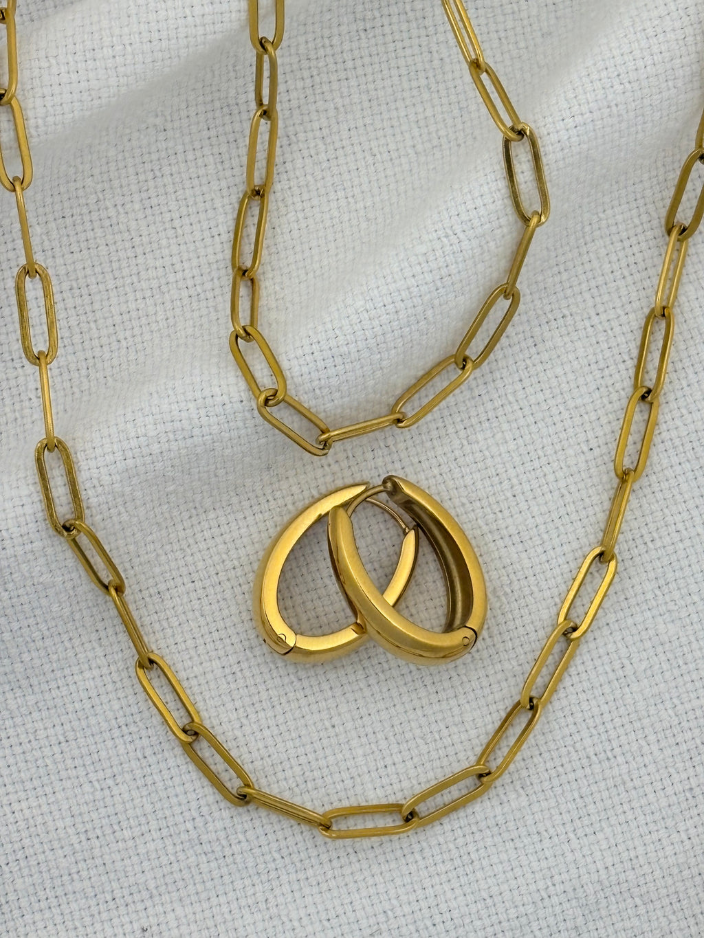 Gold chain necklace, bracelet and earrings on a textured white background