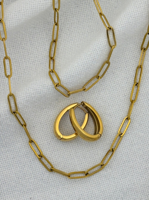 Gold chain necklace, bracelet and earrings on a textured white background