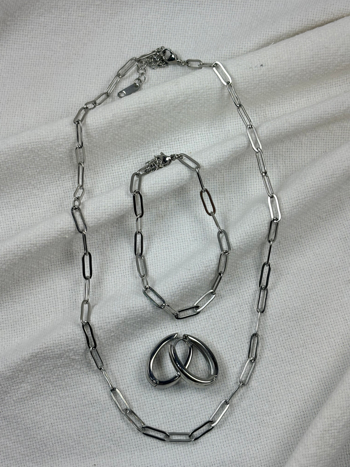 Silver chain necklace, bracelet and earrings on a light fabric background