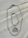 Silver chain necklace, bracelet and earrings on a light fabric background