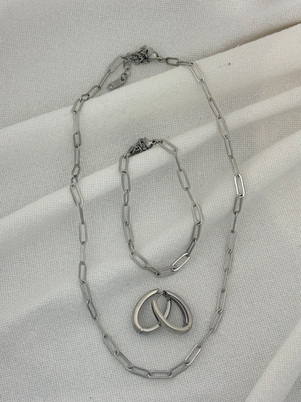 Silver chain necklace, bracelet and earrings on a light fabric background