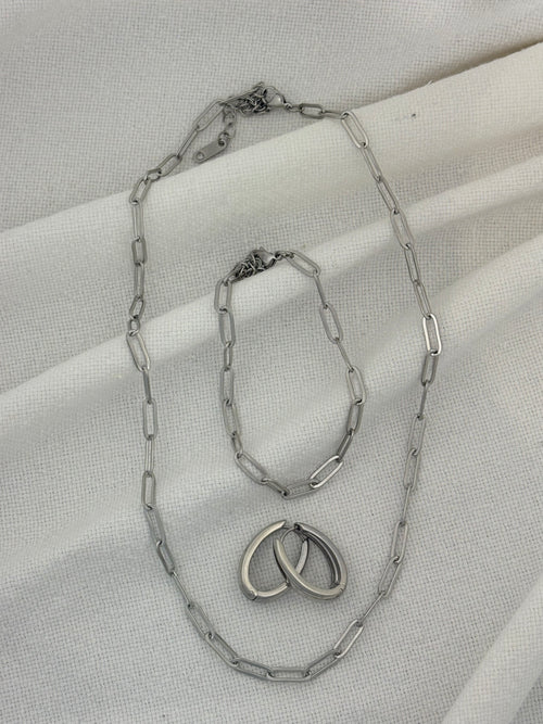 Silver chain necklace, bracelet and earrings on a light fabric background