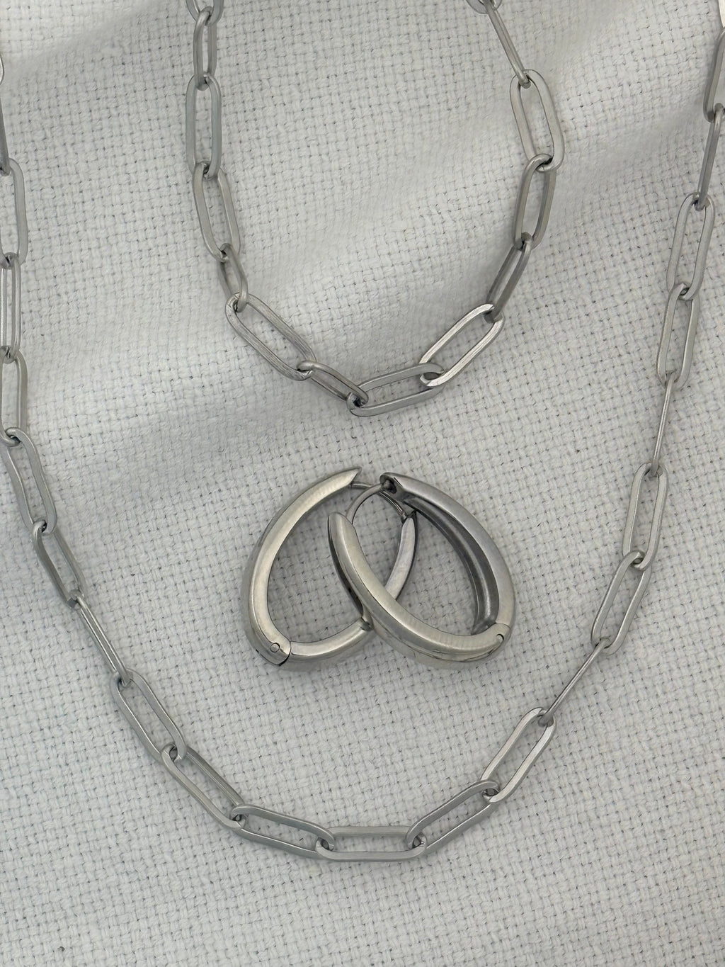 Silver necklace, bracelet and earrings on a textured gray surface
