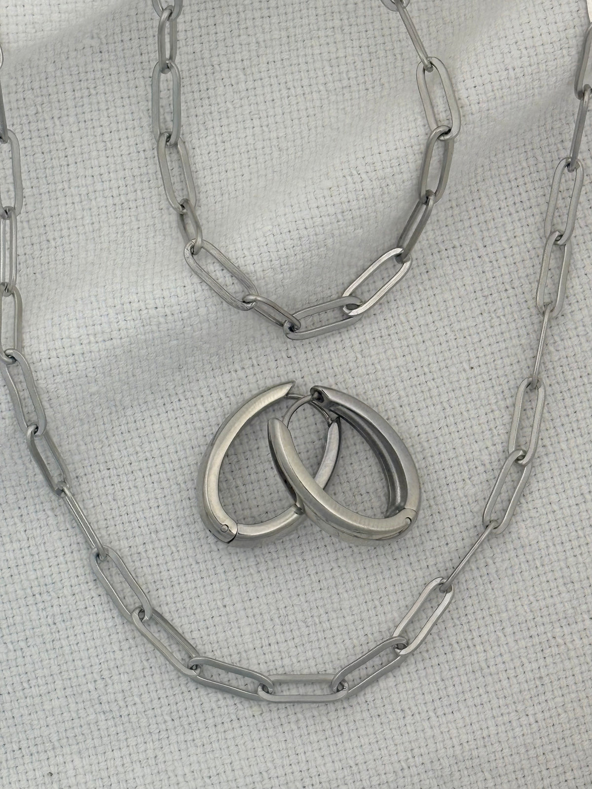 Silver necklace, bracelet and earrings on a textured gray surface