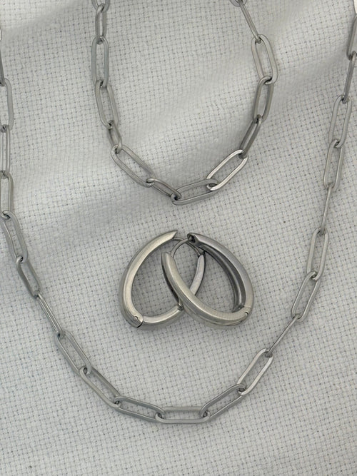Silver necklace, bracelet and earrings on a textured gray surface