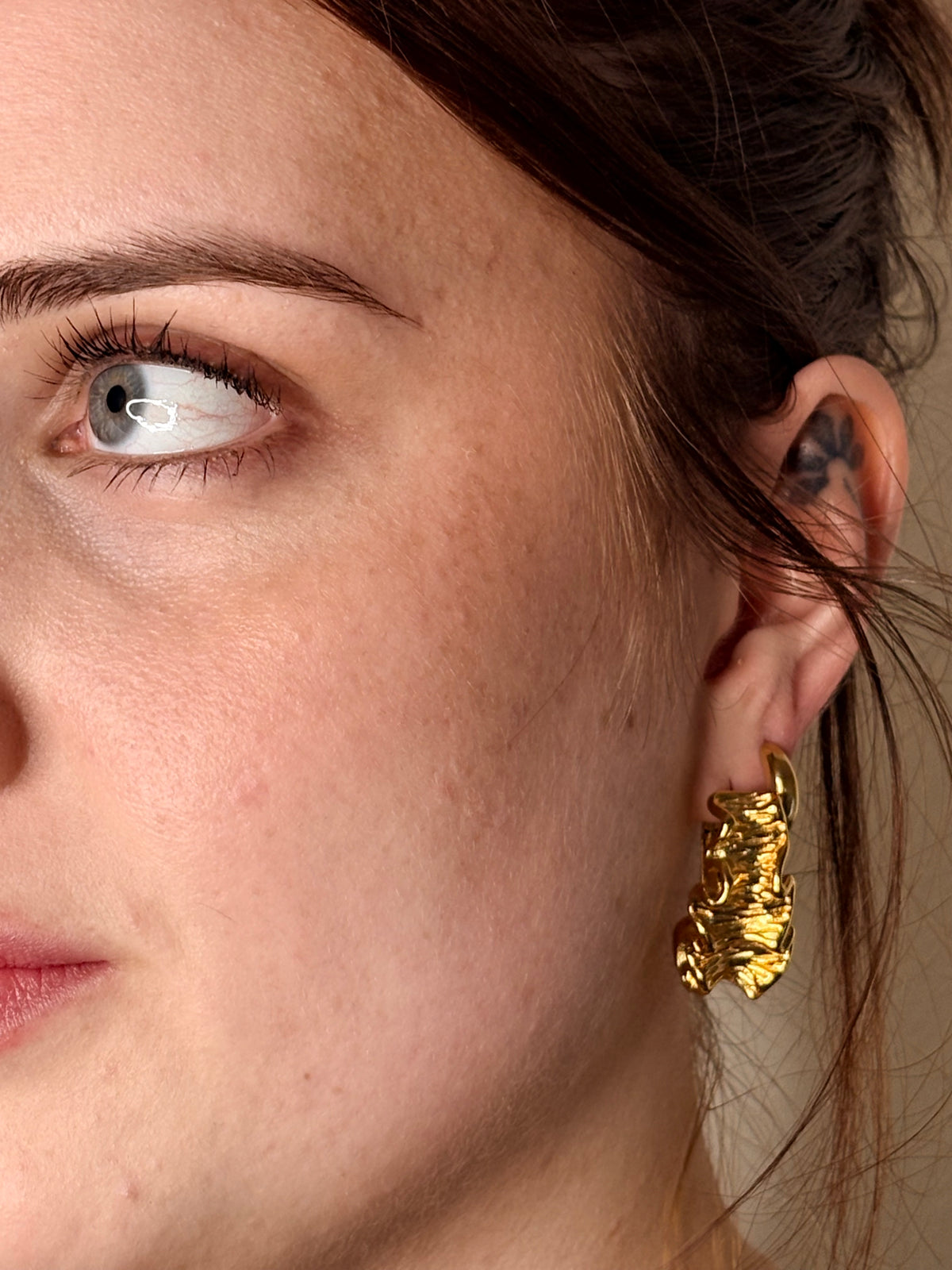 A close-up of a woman's ear wearing a chunky, textured gold hoop earring.