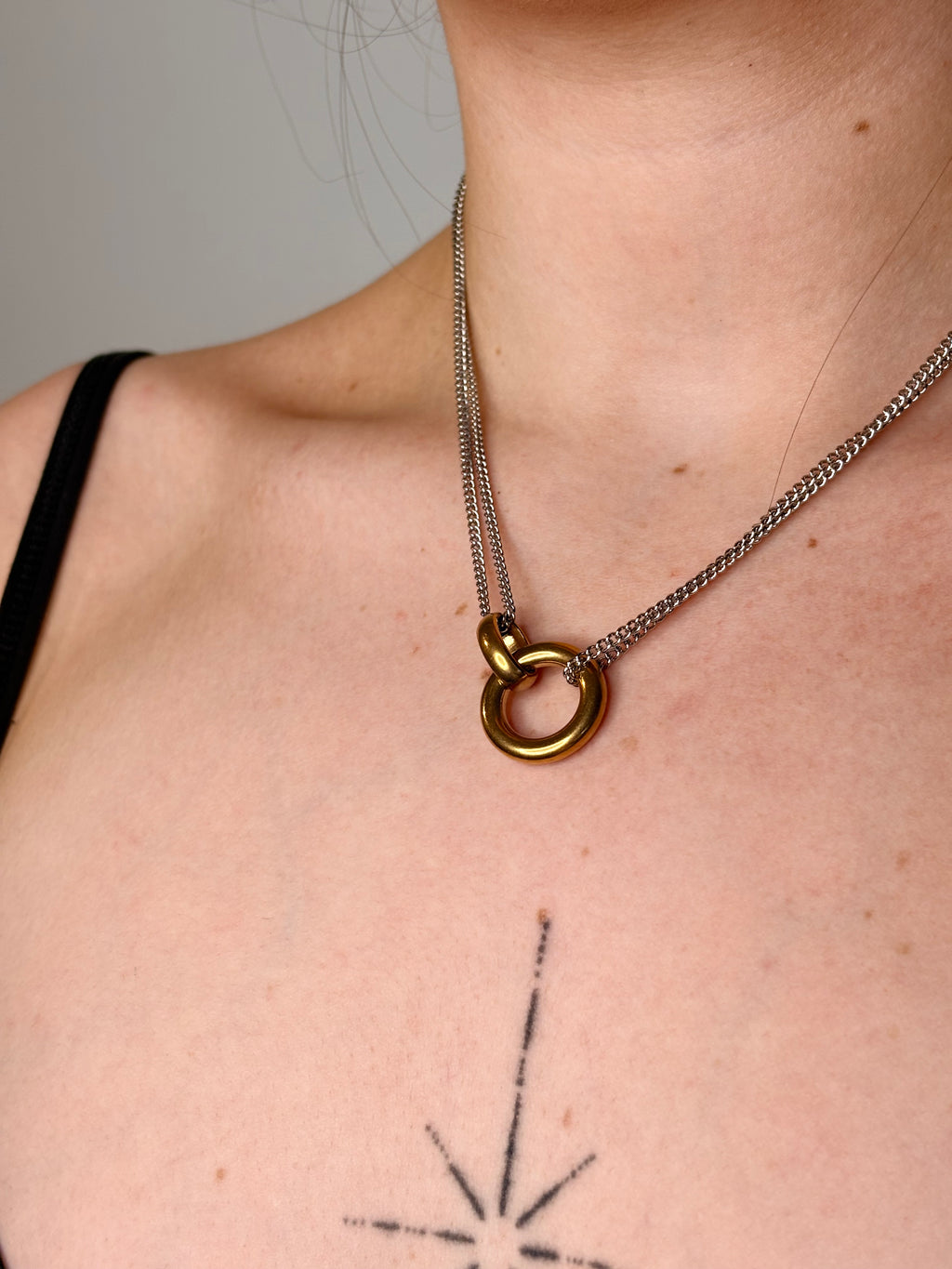 A close-up of a person's neck and upper chest wearing a silver chain necklace with a gold ring pendant.