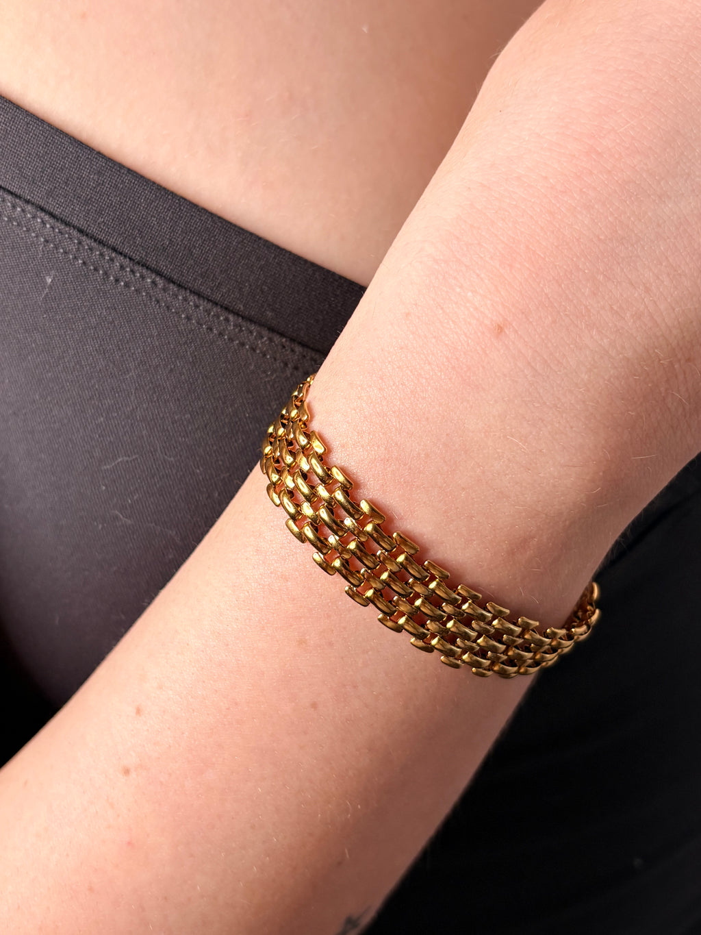 A close-up of a person's wrist wearing a gold multi-strand chain link bracelet, paired with a black top.